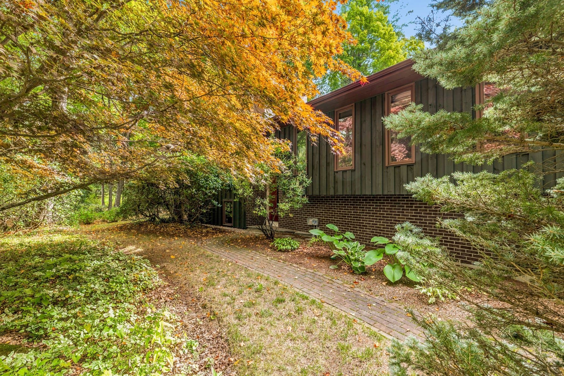 The brick front walk to the entry under the maples, with the brick foundation wall along the garden