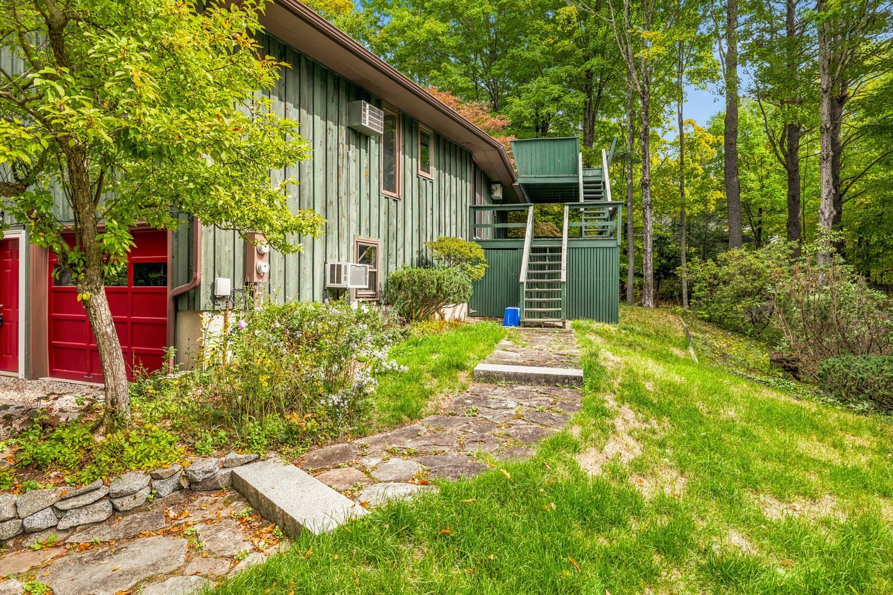The side of the house with a red door, a stone path, and the exterior stairs up to the deck