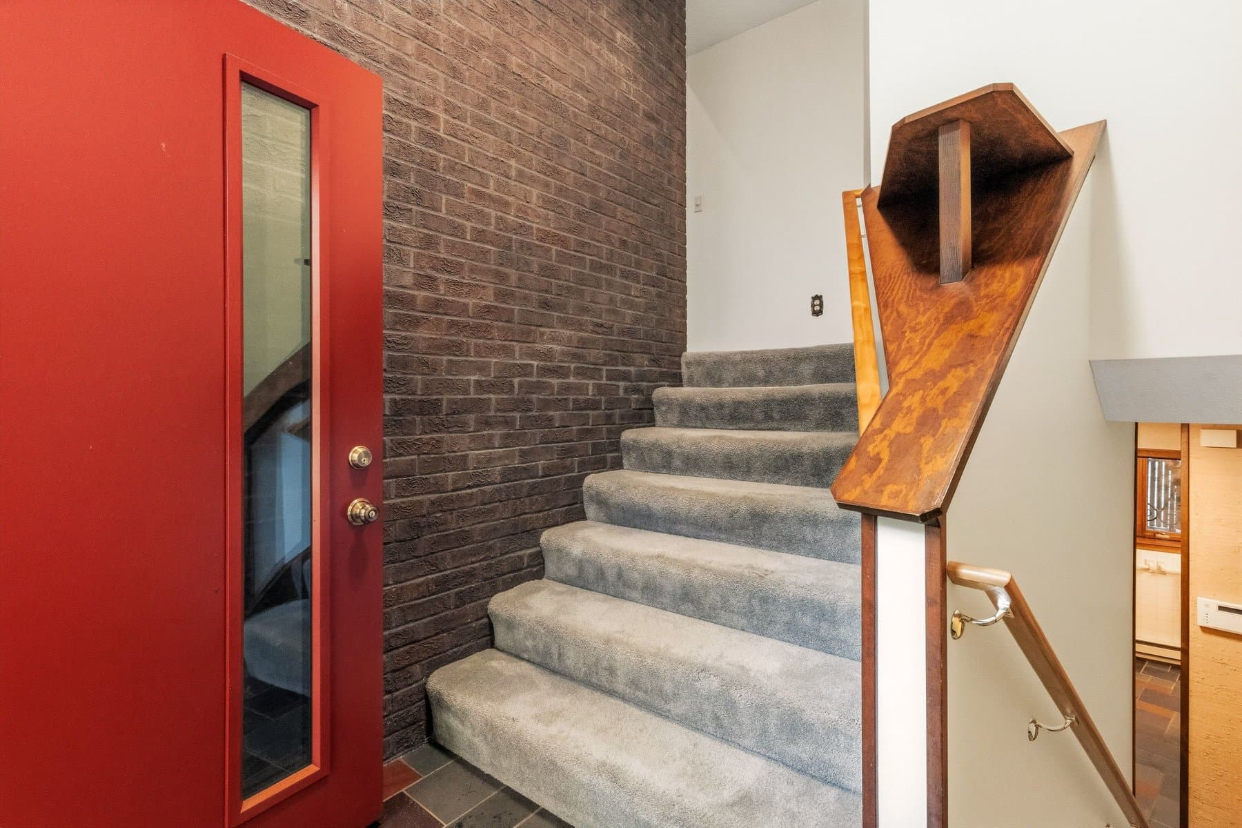 The red front door and the brick wall beside the carpeted stair with its wood newel