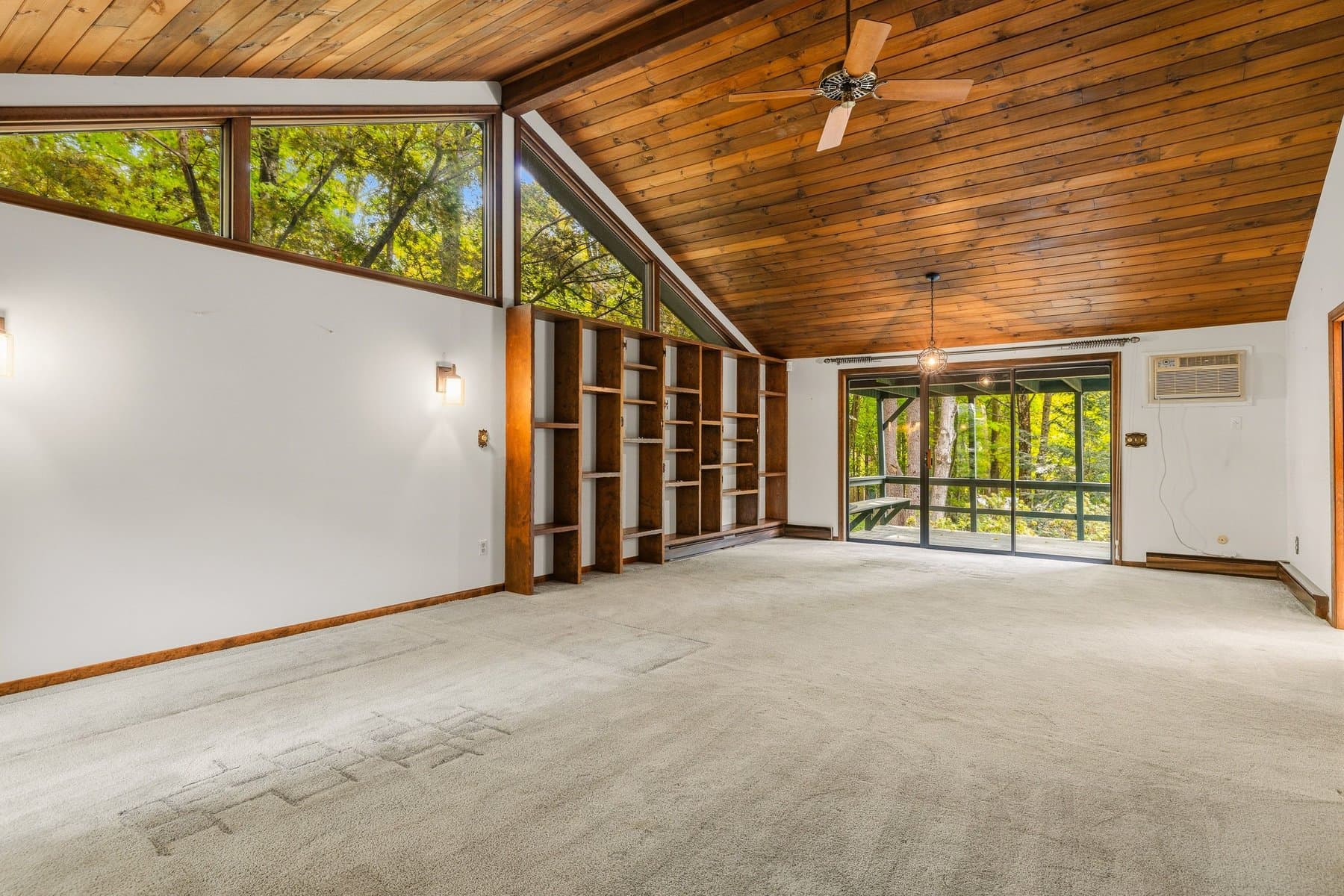 The wall of windows at the end of the living room, with the wood built-in shelving and the slider to the deck