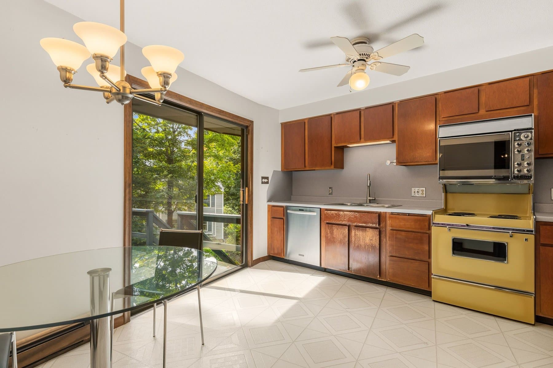 The kitchen with its original wood cabinets, the electric range, the dishwasher, and the dining nook by the slider