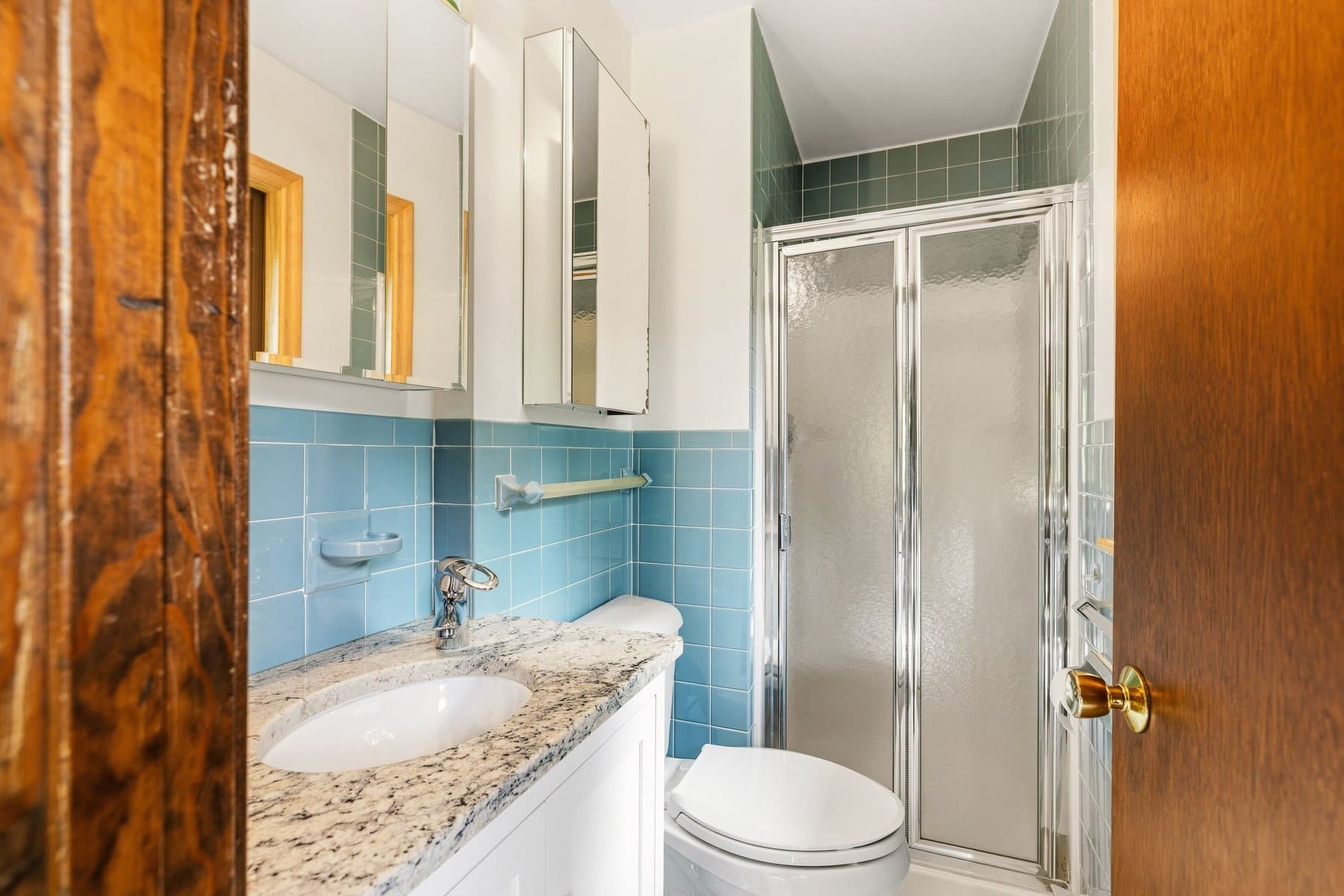 The primary bath in blue tile, with a granite vanity and a shower stall