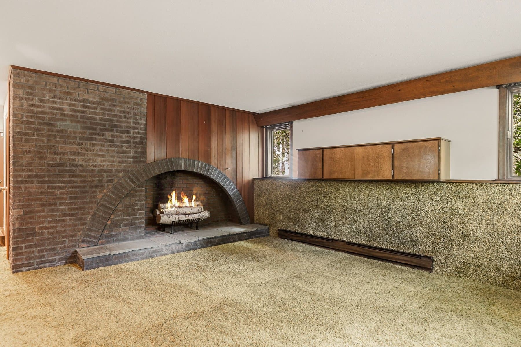 The rec room with the arched brick fireplace lit and a wood-paneled beam above