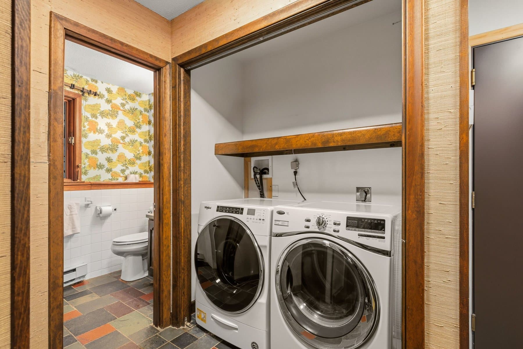 The laundry with a front-load washer and dryer on the slate floor, the lower-level bath beside it