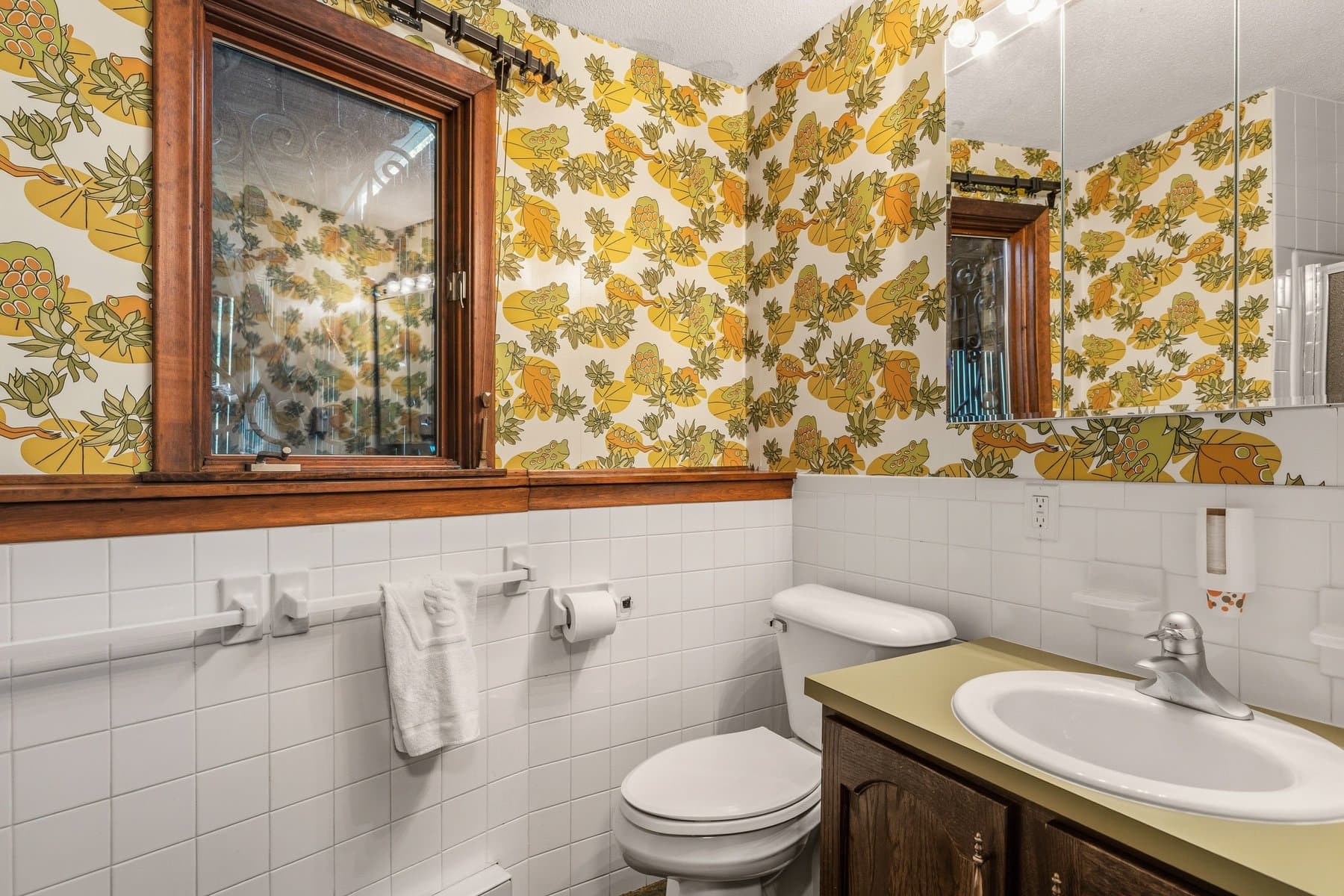 The lower-level bath with floral wallpaper, white tile, and a wood vanity